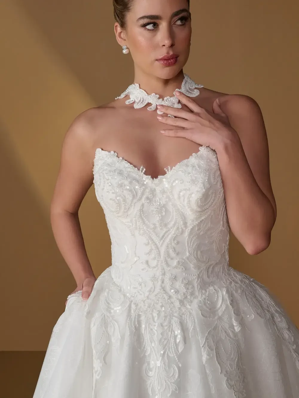 A woman in an elegant white wedding dress with intricate beadwork and a sweetheart neckline, accessorized with a matching choker.