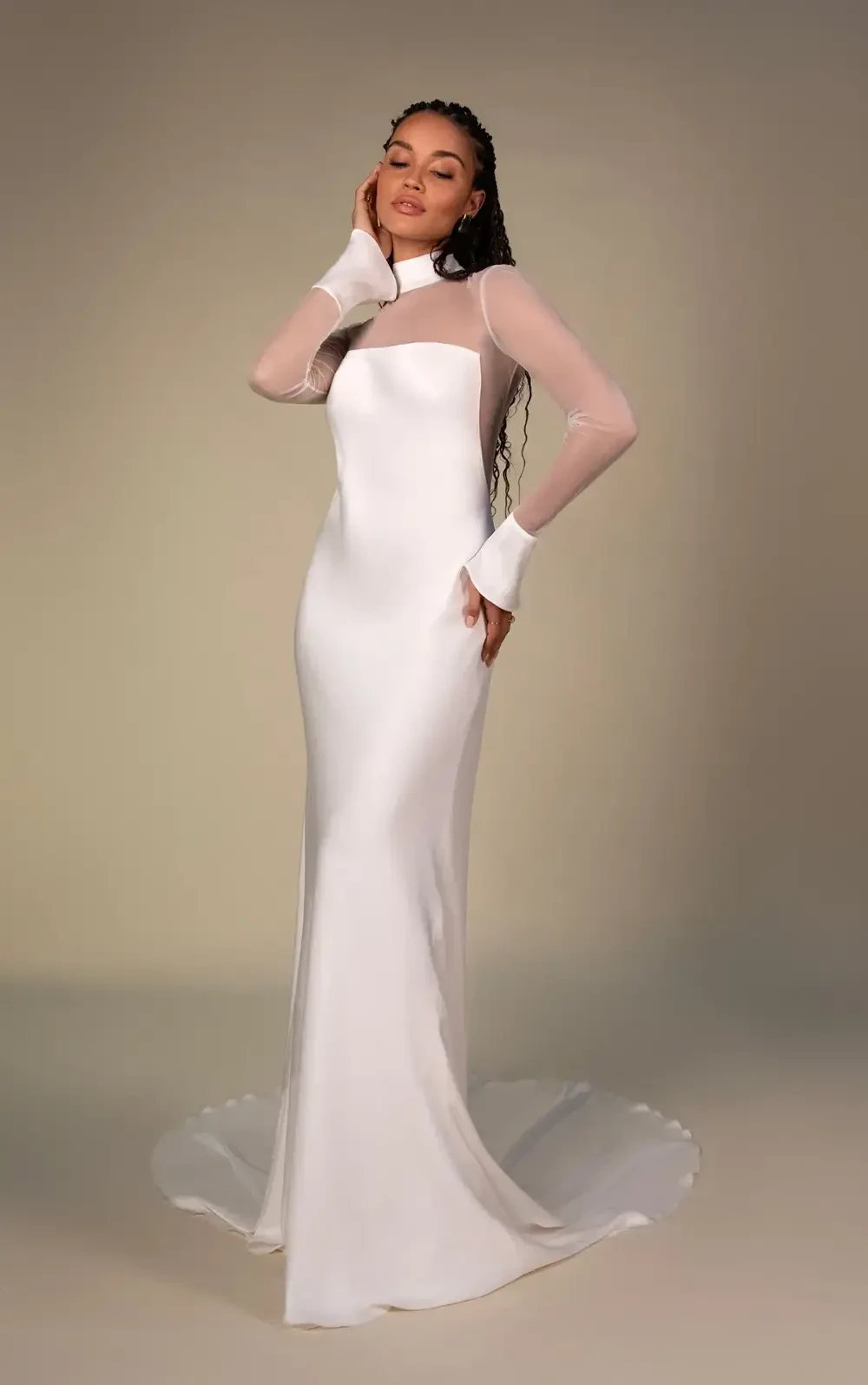 A person wearing a long, elegant white dress with sheer sleeves, posing gracefully against a neutral background.